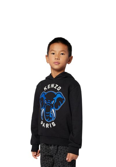 Felpa nera con grafica di un elefante blu e testi "KENZO" e "PARIS"; abbinata a pantaloni neri a fantasia.