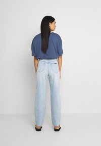 Jeans de pernas largas azul claro com bolsos traseiros em forma de coração, combinados com uma t-shirt solta azul escura. Tecido macio e design descontraído.