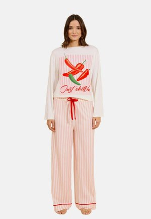 Frau trägt rosa-weiß gestreifte Pyjamahosen und ein weißes Sweatshirt mit roten und grünen Chilischoten und dem Text „Just chillin'“.