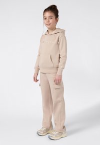 Beżowa bluza z kapturem z kieszenią kangurką i haftowanym logo, w połączeniu z pasującymi spodniami cargo z kieszeniami bocznymi oraz beżowymi sneakersami.
