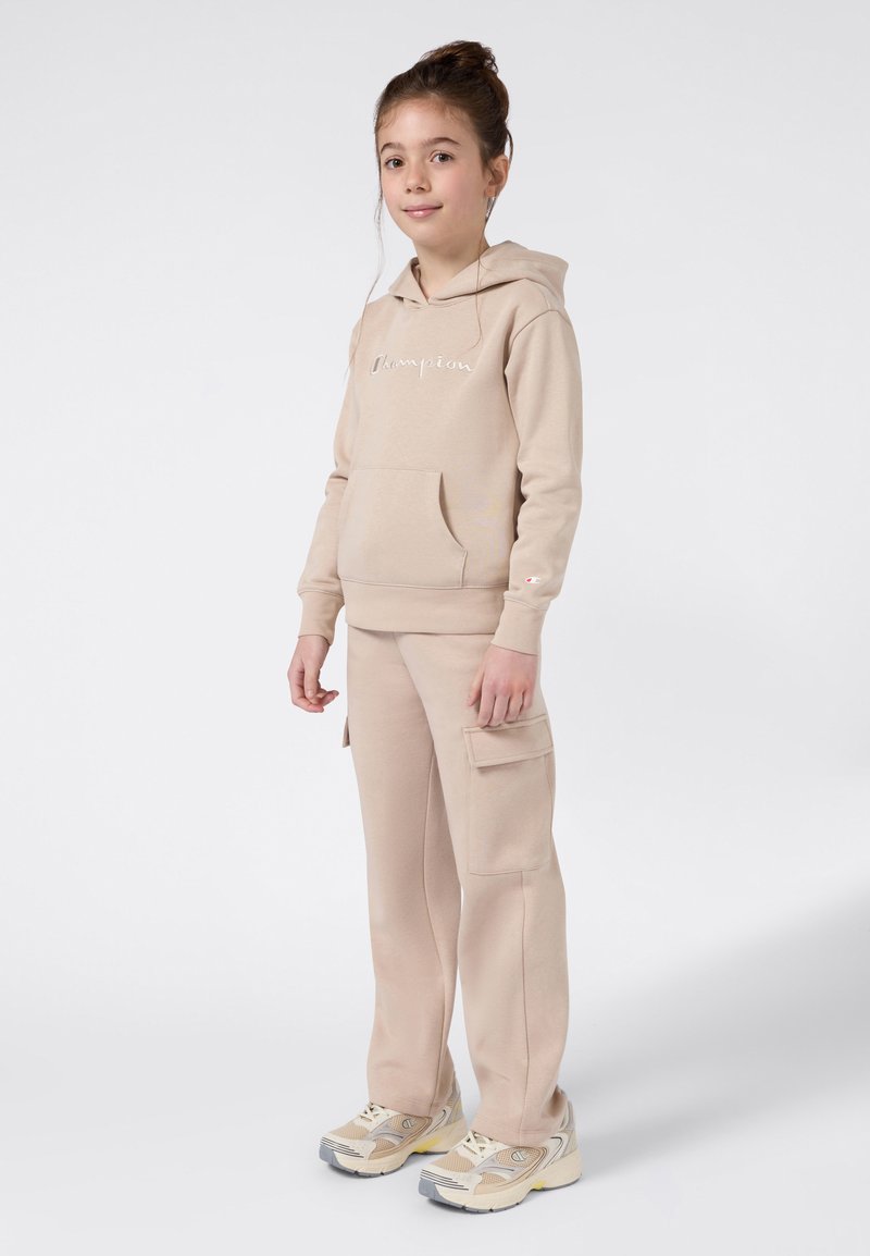 Beżowa bluza z kapturem z kieszenią kangurką i haftowanym logo, w połączeniu z pasującymi spodniami cargo z kieszeniami bocznymi oraz beżowymi sneakersami.