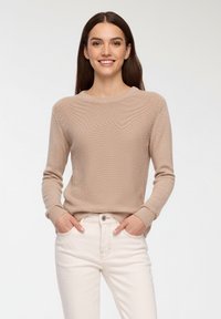 Jasno beżowy sweter dzianinowy o fakturowanym wzorze, okrągłym dekolcie i długich rękawach, zestawiony z białymi dżinsami dla kontrastowego efektu.