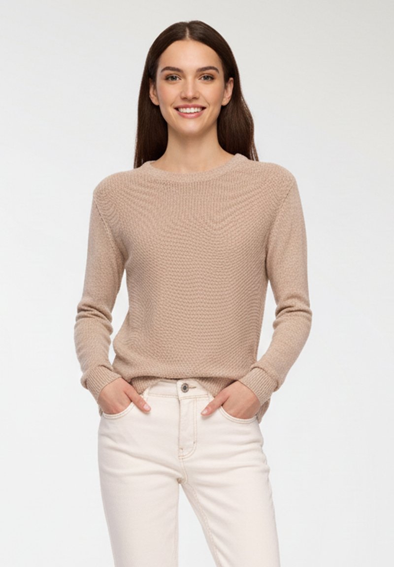 Jasno beżowy sweter dzianinowy o fakturowanym wzorze, okrągłym dekolcie i długich rękawach, zestawiony z białymi dżinsami dla kontrastowego efektu.