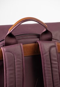 Bordeauxfarbener Rucksack mit glatter Oberfläche, ausgestattet mit gepolsterten Tragegurten und einem braunen Lederakzent auf der Rückseite. Oberer Griff für einfaches Tragen.