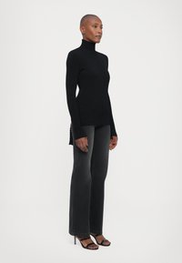 Svart rynket turtleneck-genser med lange ermer, tett passform og sideslittser. Kombinert med mørkegrå viddejeans og svarte hælsandaler.