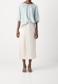 Blouse bleu clair texturé avec des manches ballons associée à une jupe longue et fluide crème. Portez-la avec des talons nus à lanières.