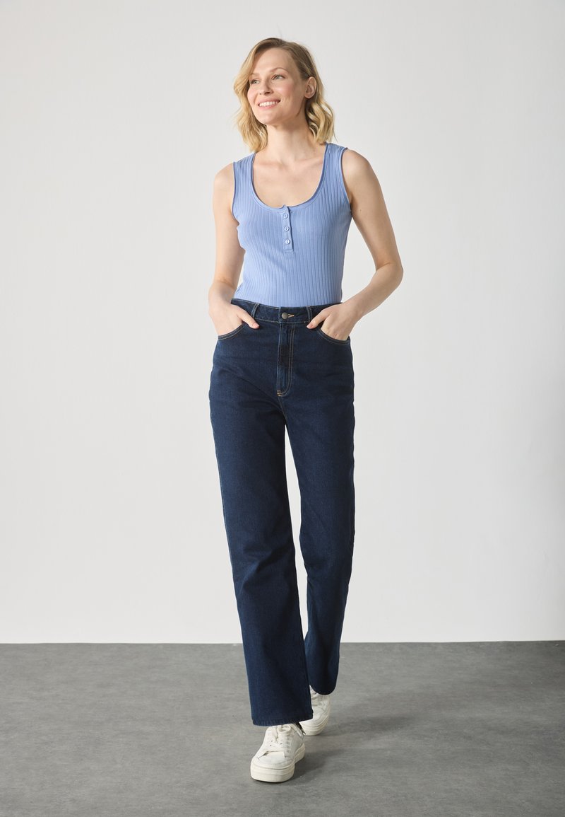 Top de tirantes azul acanalado con detalle de botones, combinado con jeans de cintura alta de color azul oscuro y zapatillas blancas. Silueta sencilla y ajustada, de estilo casual.