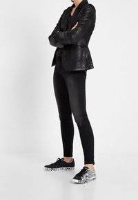 Blazer noir texturé avec une coupe ajustée, associé à un jean skinny noir et à des baskets noires avec du texte blanc audacieux sur les côtés.