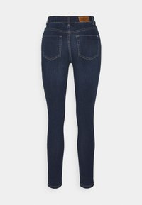 Jeans skinny de mezclilla azul oscuro con una cintura alta, cinco bolsillos y una etiqueta de cuero con la marca en la parte posterior. Textura suave, diseño ajustado.