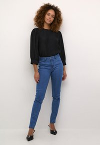 Mustvalge kangas, millel on puhvli varrukad, koos kõrge vöökoha siniste kitsaste teksade ja mustade terava ninaga mules'itega. Neutraalne taust.