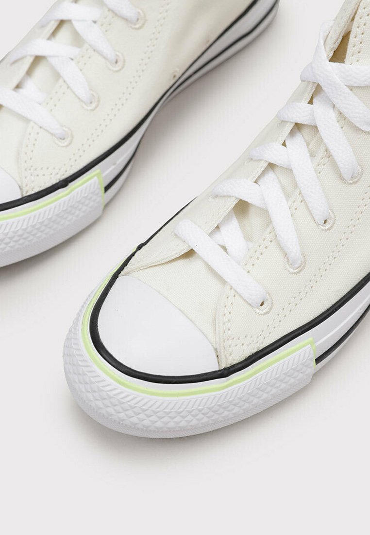 Sneakers in tela di colore avorio con lacci bianchi e suole in gomma. Presentano un accento verde lungo la suola e una striscia nera vicino alla base.