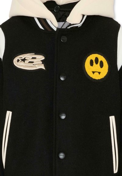 Giacca varsity nera realizzata in misto lana, con cappuccio crema. Include toppe ricamate: una lettera e una faccina sorridente gialla. Dettagli bianchi.