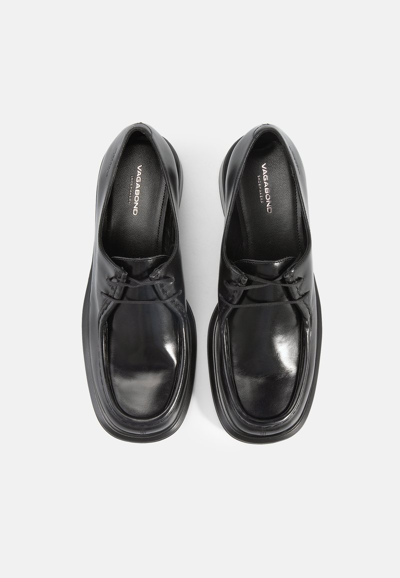 Zapatos de cuero negros con forma redondeada, textura suave y detalles de costura. Presentan un tacón bajo y acentos elásticos para un mejor ajuste.