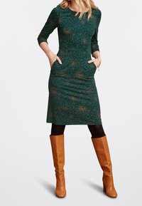 Grön klänning med guldprickar, trekvartsärmar, figursydd passform, knälång. Kombinerad med bruna knähöga stövlar. Två sidofickor.