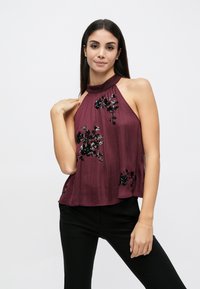 Μπουρντό κορυφή με halter και κεντήματα με λουλούδια, με άνετη εφαρμογή και υφή υφάσματος. Διακοσμητικά στοιχεία περιλαμβάνουν παγιέτες και υψηλό λαιμό.