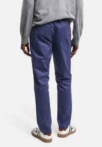 Marineblaue Chinos mit geradem Bein, aus weichem Material gefertigt, mit zwei Gesäßtaschen und einer glatten Oberfläche. Kombiniert mit Sneakers.