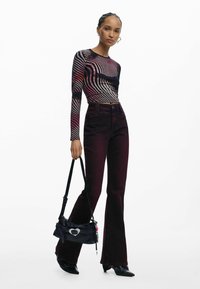 Długi rękaw, drukowana bluzka w faliste linie w kolorze czerwonym i czarnym, zestawiona z bordowymi dzwonami i małą czarną torebką z srebrnymi akcentami.