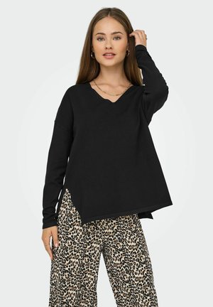 Haut noir à manches longues avec un col en V et un ourlet asymétrique, associé à un pantalon beige à motif léopard.
