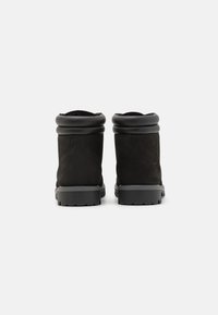 Botines de ante negro con puño enrollado, suela de goma y detalles de costura en los costados. Textura suave sin patrones visibles.