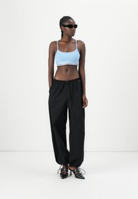 Calvin Klein blauwe crop top met witte logo-band, gecombineerd met zwarte, losse joggerbroeken. Model draagt zwarte zonnebril en schoenen met hak.
