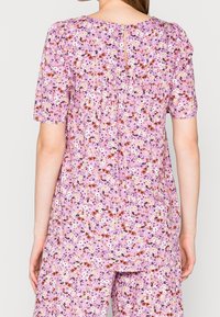 Floral-patterned blouse in light pink, featuring short puff sleeves, a keyhole back closure, and subtle pleats at the back for detail.