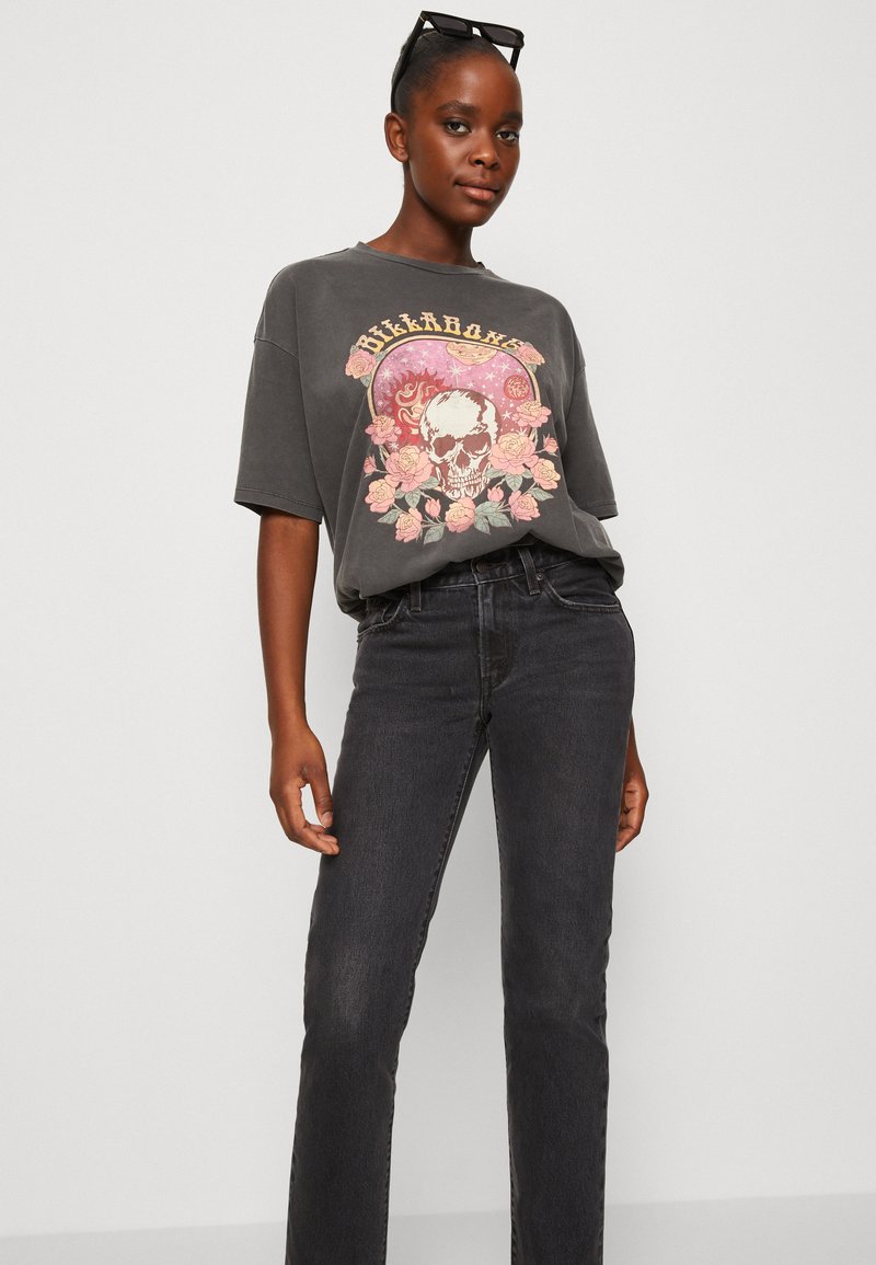 T-shirt gris oversize avec un motif crâne floral, associé à un jean noir taille haute. Tissu doux, coupe décontractée, manches courtes.