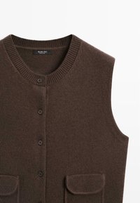 Gilet tricoté marron sans manches avec col rond, boutons sur le devant et deux petites poches à rabat sur fond blanc.