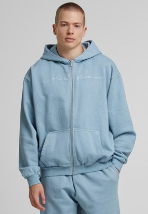 Lyseblå zip-hoodie lavet af en bomuldsblanding. Har forlommer, ribbet manchetter og kant, samt broderet logo på brystet.