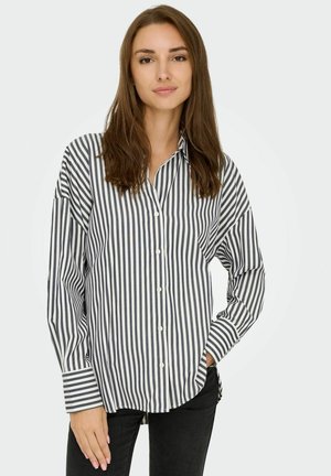 Camicia a righe blu e bianca, realizzata in tessuto, con maniche lunghe, colletto e una vestibilità rilassata. Jeans neri completano l'outfit.