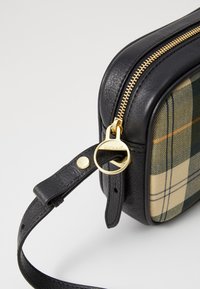 Saco de couro preto com lado em tecido xadrez. Detalhes em zíper dourado e anel metálico. Alça ajustável em couro preto. Textura suave.