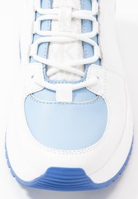 Vit och ljusblå sneaker med en slät läderöverdel, textillaces och texturerad gummisula; har en rundad tå och sömdetaljer.