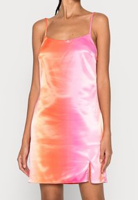 El vestido de satén presenta un diseño degradado que pasa de rosa a naranja. Tiene tirantes finos y una abertura lateral cerca del dobladillo.