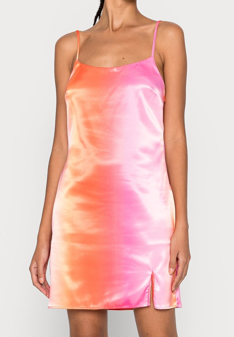 El vestido de satén presenta un diseño degradado que pasa de rosa a naranja. Tiene tirantes finos y una abertura lateral cerca del dobladillo.