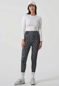 Dugi bijeli crop top s dugim rukavima, sive tajice s uzorkom leoparda, bijele čarape s crnim tekstom i sive sportske tenisice. Jednostavan dizajn, prilagođeni stil.