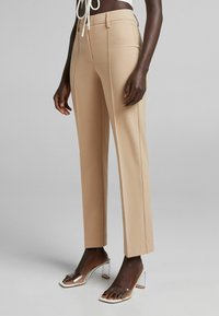 Beige přizpůsobené kalhoty se slim fit, rovnými nohavicemi a podélným skladáním v přední části. V kombinaci s průhlednými sandály na podpatku. Hladká textilie.