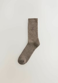 Brauner, gerippter Socken mit einem violetten Logo an der Seite. Verfügt über eine gepolsterte Sohle und eine glatte Textur. Standardlänge bis zum Knöchel.