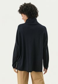 Navyblauw, oversized coltrui van zacht materiaal. Kenmerkt zich door verlaagde schouders en geribbelde manchetten. Gecombineerd met lichtbruine broeken.