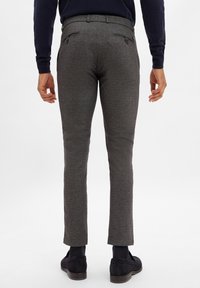 Graue, maßgeschneiderte Hosen aus strukturiertem Stoff, schlanke Passform und zwei Gesäßtaschen. Getragen mit dunklen Schuhen und einem marineblauen Pullover.