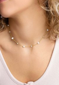 Guldtonad halsband med tvinnad kedja, prytt med små runt pärlor som är jämnt fördelade längs längden. Enkel design, lämplig för lager-på-lager styling.
