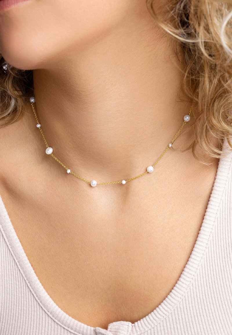 Guldtonad halsband med tvinnad kedja, prytt med små runt pärlor som är jämnt fördelade längs längden. Enkel design, lämplig för lager-på-lager styling.