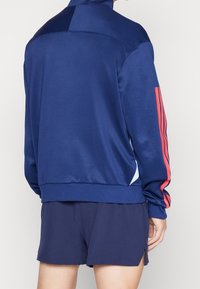 Person wearing navy blue athletic jacket with red stripes on sleeves and matching navy shorts, shown from the back.