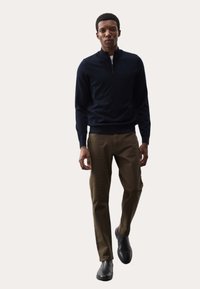 Granatowy sweter z zamkiem na szyi i długimi rękawami w połączeniu z khaki, dopasowanymi spodniami oraz czarnymi skórzanymi botkami. Gładkie kolory, gładka tekstura.