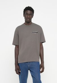 T-shirt en coton gris à manches courtes présentant un col rond et un petit logo imprimé sur le côté gauche de la poitrine. Design simple avec une coupe décontractée.