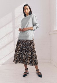 Pilkas džemperis su ilgomis rankovėmis, derinamas su rudomis gyvūnų rašto plytomis sijonu. Ant kojų – juodi smailūs batai su kulkšnies dirželiais.