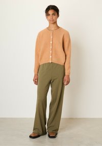 Oranž mohair-segu cardigan ümmarguse kaelusega, ees nupulukuga ja pikkade varrukatega. Kombineeritudoliivroheliste laiade pükstega ja pruunide baleriinadega.