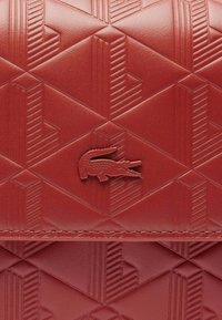 Portefeuille texturé rouge avec un motif géométrique en relief, une couturer piquée et un accent de logo de crocodile bien en vue.