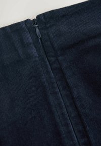 Tissu en velours côtelé bleu marine à texture lisse, doté d'une fermeture éclair dissimulée dans le dos, créant une silhouette ajustée.