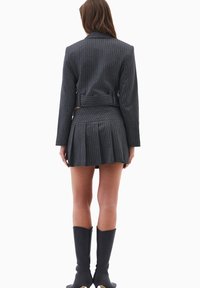 Grå stribede blazer med matchende plisseret nederdel. Stoffet ser glat ud; har en belted talje og knælange sorte støvler.