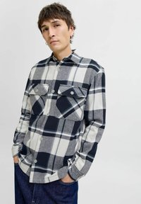 Camisa a cuadros en azul marino, blanco y gris, que presenta un diseño de botones, dos bolsillos en el pecho y un cuello clásico. Hecha de una tela suave.