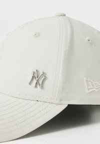 Cappellino da baseball bianco con un piccolo logo intrecciato "NY" in argento sulla parte frontale e un emblema ricamato sul lato.
